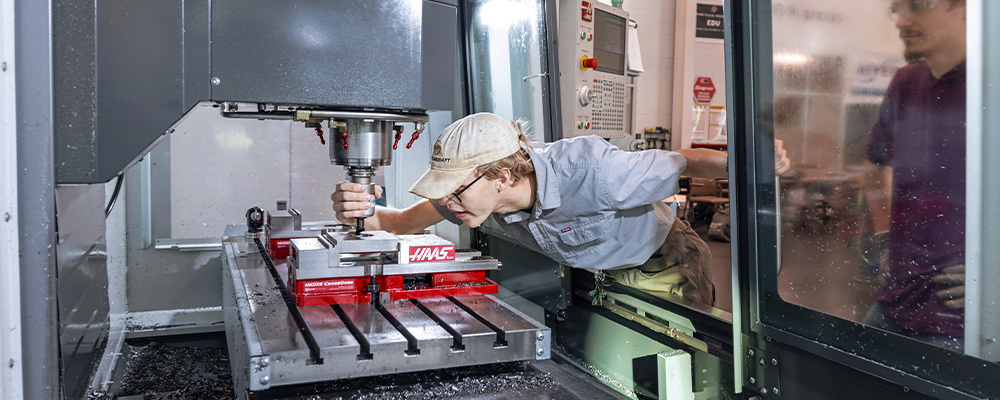 A male student leans into the machine to inspect