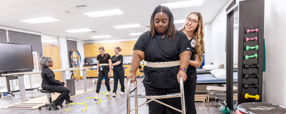 A girl helping a classmate in a practice excercise with the intructor and two other students in the back