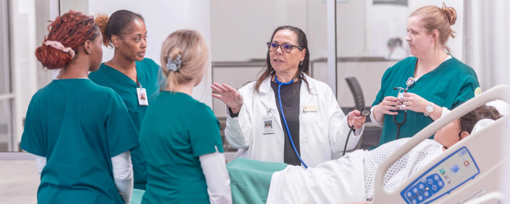 A nursing instructor with four female students demonstrating on a interactive dummy in a lab