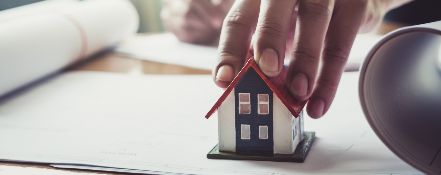 A hand placing down a house on top of blueprint sheets